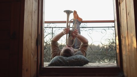 a man plays a trumpet on the balcony. there's a pillow under your head, feet up. freelancing and idleness during the pandemic. freedom of expression.