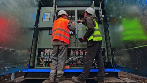 Engineers connect electrical system outdoors. Two electricians in protective uniform checking voltage on the solar power plant.