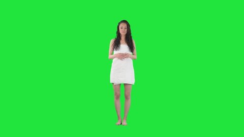 Slow motion of young woman wrapped in white towel touching freshly showered wet hair.  Full body isolated on green screen chroma key background.