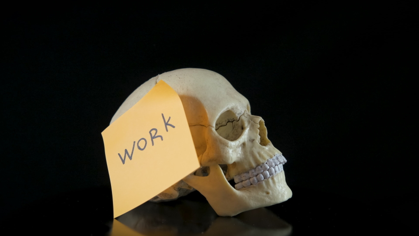 Risk from exhausting work. A spooky skull with the sticker with the word work writing on it against the black bakcground.