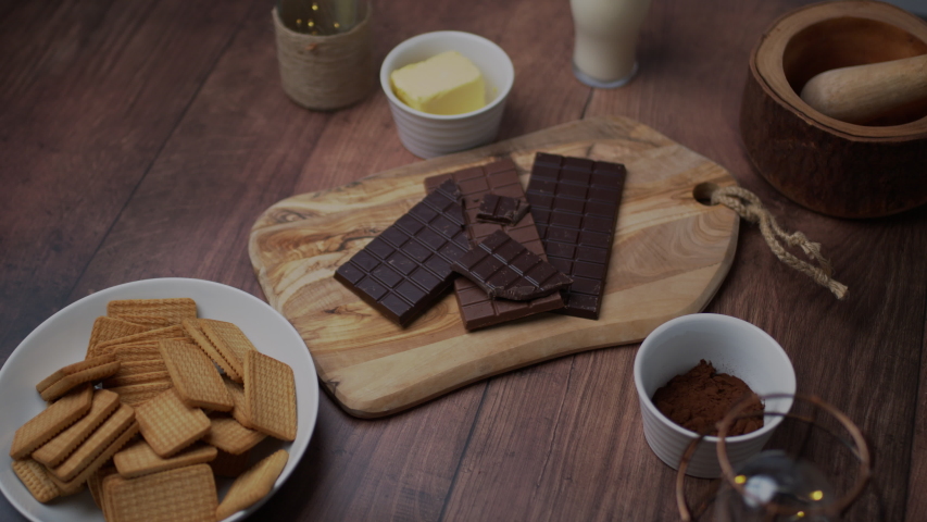 Chocolate cake ingredients: Malted Milk biscuits, a bowl of Cacao, a glass of Buttermilk, a piece of Butter, a bunch of milk and dark Chocolate on the wooden dark table.