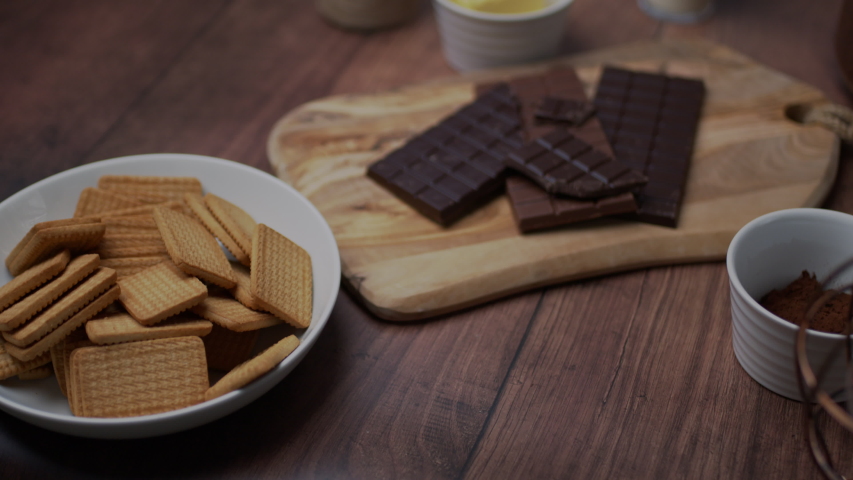 Chocolate cake ingredients: Malted Milk biscuits, a bowl of Cacao, a glass of Buttermilk, a piece of Butter, a bunch of milk and dark Chocolate on the wooden dark table.
