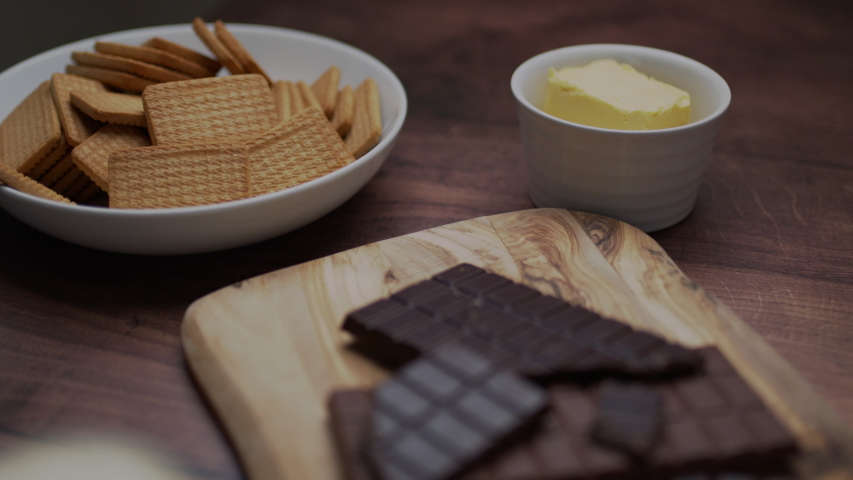 Chocolate cake ingredients: Malted Milk biscuits, a bowl of Cacao, a glass of Buttermilk, a piece of Butter, a bunch of milk and dark Chocolate on the wooden dark table.