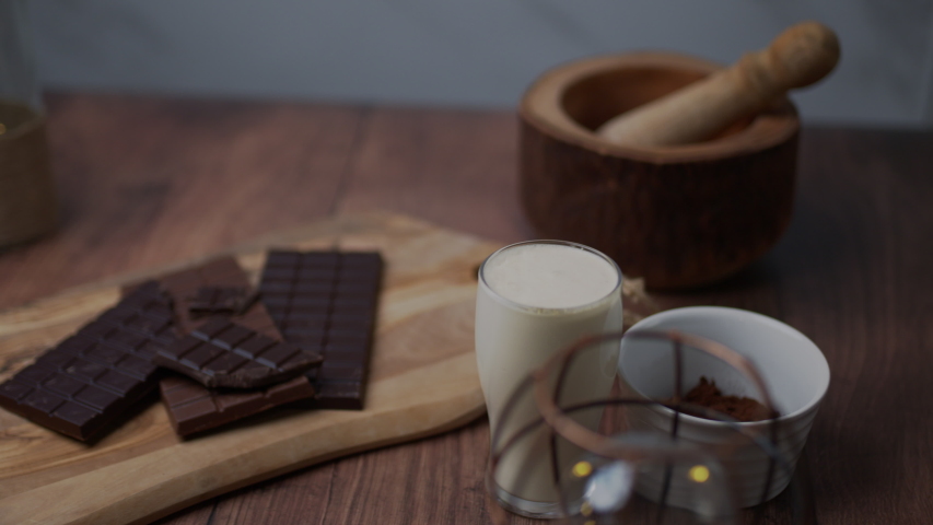 Chocolate cake ingredients: Malted Milk biscuits, a bowl of Cacao, a glass of Buttermilk, a piece of Butter, a bunch of milk and dark Chocolate on the wooden dark table.