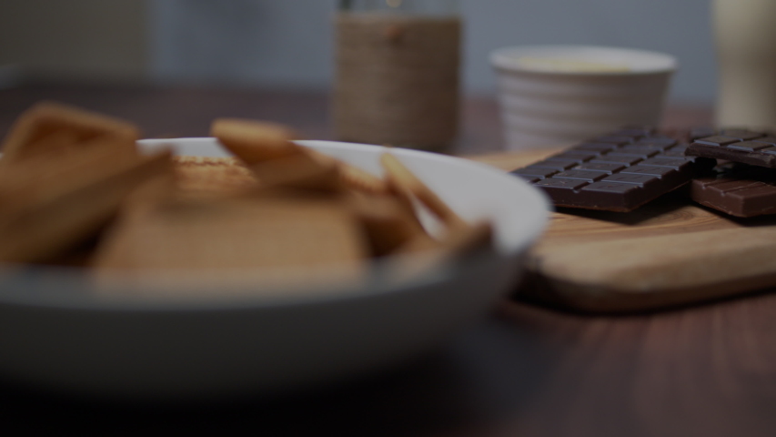 Chocolate cake ingredients: Malted Milk biscuits, a bowl of Cacao, a glass of Buttermilk, a piece of Butter, a bunch of milk and dark Chocolate on the wooden dark table.