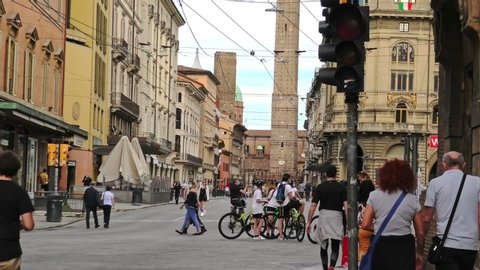 Bologna, Italy - May 9, 2020: Italian families with the surgical masks walking and riding bikes on the road with two towers on the background. Covid-19 with social distancing after lockdown