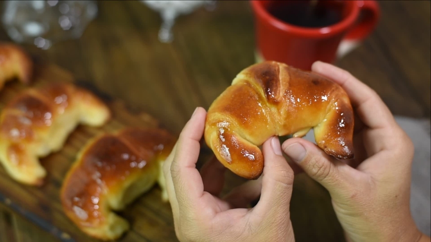 
hands opening a fresh and tender homemade croissant on table prepared for breakfast or snack