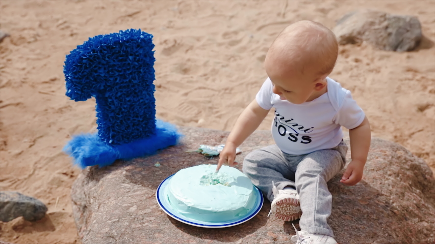 Little baby boy touches birthday cake with number one on beach