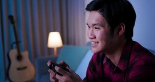 asian man use gamepad and play video games happily in the evening at home