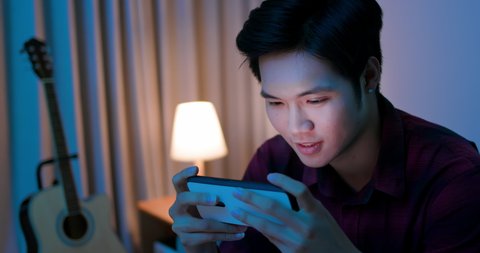 asian man use smart phone and play mobile games on sofa at home