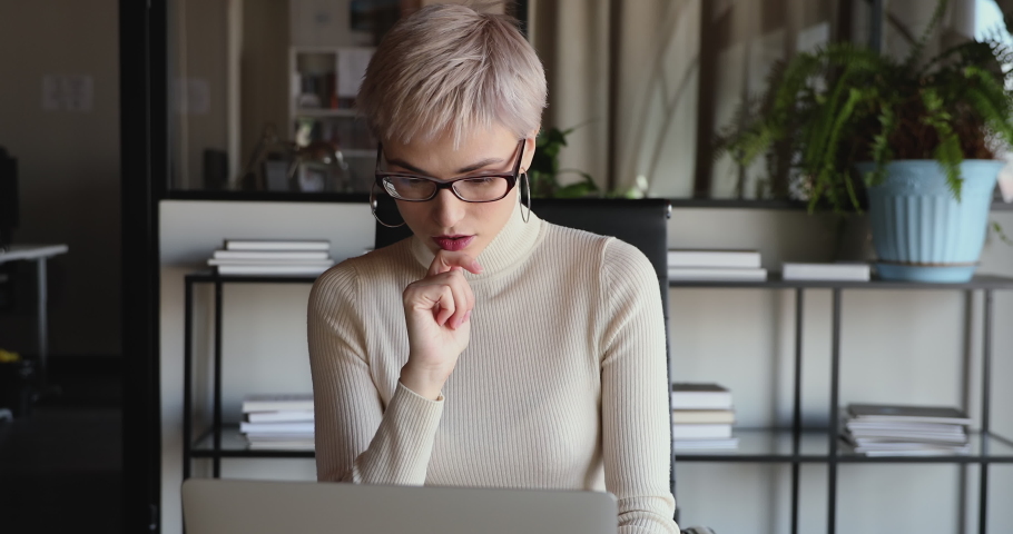 Young serious business woman thinking of business challenge. Anxious female executive feeling concern or doubt, making difficult decision, searching online problem solution in office using laptop. | Shutterstock HD Video #1052249086