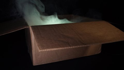 A cardboard box from which smoke comes and light shines. Concept of sorcery and magic. Black background