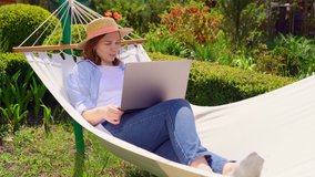 female businesswoman freelancer lies in the hammock and working on the computer, answering a live video phone call, makes a selfie photo. Remote working, isolation in quarantine. the social distance.