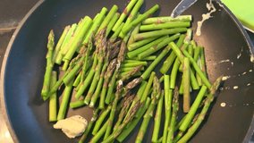 Cooking green asparagus sprouts on a pan. 4k closeup video of preparing food