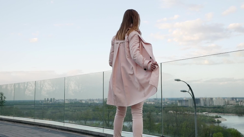 Beautiful attractive cute girl in a good mood on the observation deck in pink with a happy look is spinning in the wind. Slow motion