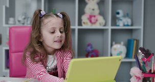 Girl plays a game on a tablet and looks at the camera. Kid girl using digital tablet technology device. Small child hold pad computer play game at home. Children tech addiction concept