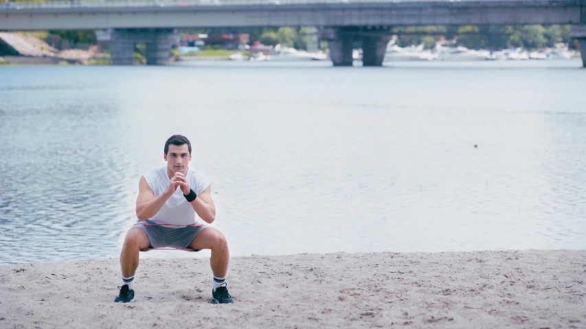 young, athletic sportsman doing side stepping and ups on river shore