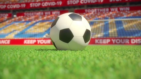 Close-up of a football or soccer ball on grass in an empty stadium with stop covid-19 slogans. Ghost games without fans during coronavirus pandemic concept. Realistic high quality 3d animation.