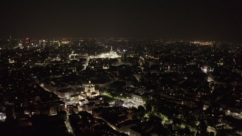 Aerial view of downtown Milan, Italy with Duomo cathedral and Porta Nuova skyscrapers seen from drone flying in the sky at night. Italian city landscape in Milano with buildings and streets