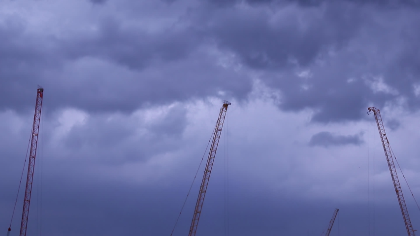 Resting construction tower crane jibs and floating dark blue gray clouds in the sky