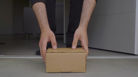 Delivered Cardboard Box Package on the Porch, Anonymous Man Picks-up His Postal Parcel. Close-up Low Ground Level Shot. man in socks and black suit, minimal scene