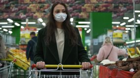 Young woman wearing protective medical face mask rolls shopping cart at grocery store. Female customer picks vegetables at economy supermarket during covid-19 coronavirus pandemic, social distancing - Powered by Shutterstock - Get 15% off with code: PIKWIZARD15