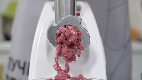 Filling comes out through raw meat grinder sieve. Grinder close up. Pile of chopped meat. Electric mincer machine with fresh chopped meat. Preparation of minced beef with an electric meat grinder.