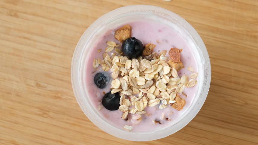 Fruit yogurt with muesli and blueberries in plastic jar, top view. Mixing muesli with yogurt. Clean eating, healthy lifestyle concept