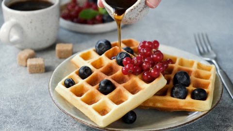 Syrup pouring on belgian waffles served with berries. Sweet sugar waffles with maple syrup