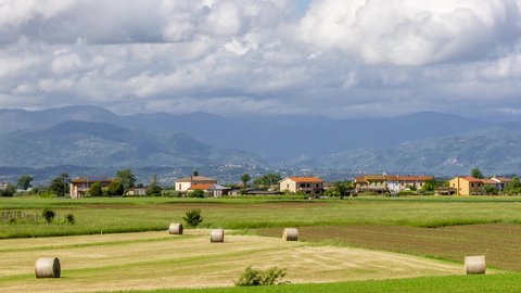Beautiful landscape of the Tuscan countryside between the provinces of Pisa and Lucca, with hay bales in the foreground and Mount Abetone in the background, Italy, with moving clouds