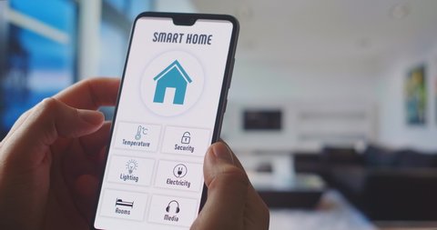 Smart home, application on the phone. A man manages various parameters of his home from a smartphone. Smart home. Man holding phone with app smart home on screen in room house