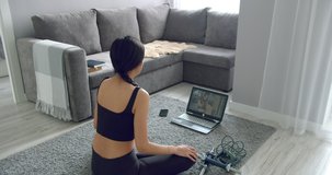 Sporty young woman doing stretching exercises while watching fitness video online on laptop at home. Healthy lifestyle concept. Sports during self-isolation.
