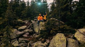 Young man and woman sitting on a rock on top of a mountain and taking a selfie. Visualization of Information Flows and Lines Flying from Mobile Phone into Global Network. Aerial Drone Shot - Powered by Shutterstock - Get 15% off with code: PIKWIZARD15