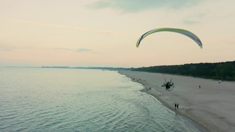 
Aerial shot of a motorized paraglider / paramotor above the sandy beach of the Baltic Sea, near many tourist hotels and buildings in orange sunset.