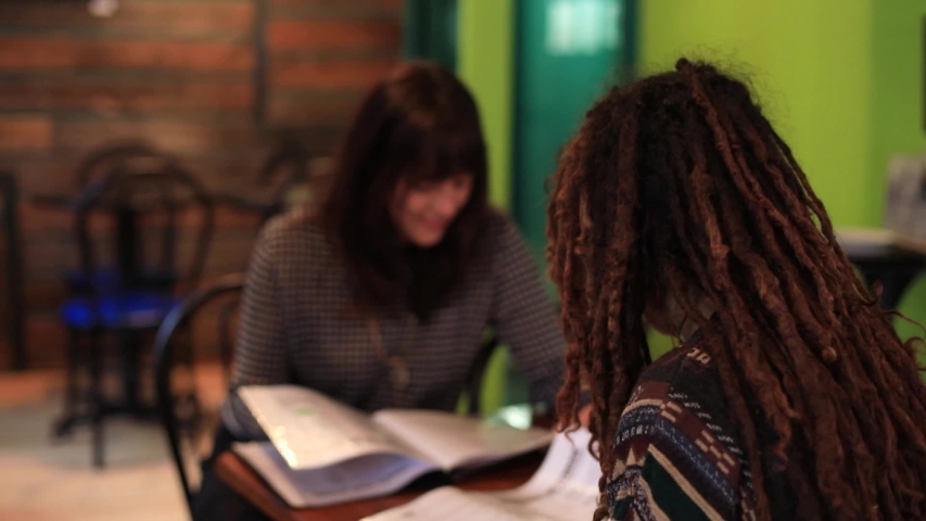 Selective rear view shot of young female friends sitting in modern, restaurant looking at menu book to decide cuisine and food to order for lunch