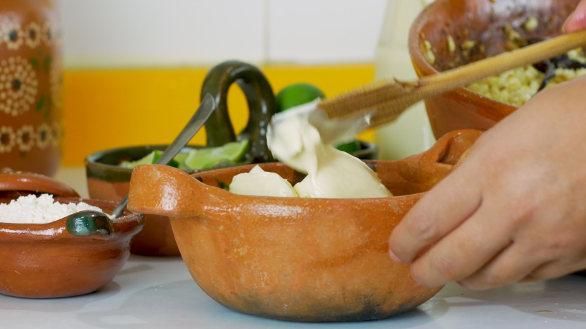 Young woman pours corn kernels and mayonnaise to prepare Mexican Street Corn Salad (Esquites) into traditional clay dish Royalty-Free Stock Footage #1052314720