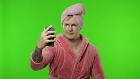 Portrait of young man wearing pink bathrobe and eye patches after shower doing beauty procedures and using smartphone social network app for video call. Funny-looking. Chroma key
