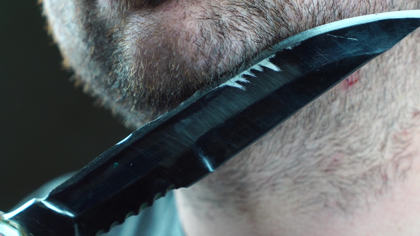 A man tries to shave his beard hunting knife close-up black background