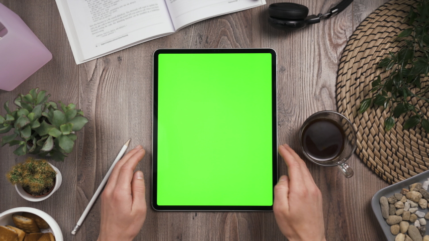 Big tab with chroma key green screen on it lay on the workplace table. Hand swipe left on touchscreen. Big screen of the tablet. Right hand swiping left. Work table with many things on it. Day time Royalty-Free Stock Footage #1052318878