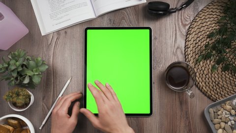 Big tab with chroma key green screen on it lay on the workplace table. Hand swipe left on touchscreen. Big screen of the tablet. Right hand swiping left. Work table with many things on it. Day time