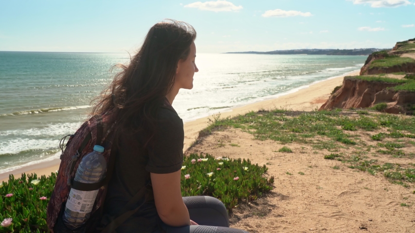A successful, happy young girl, on a cliff near the ocean, tired of a walk, sat down to rest on a stone. Portugal. Vilamoura.
