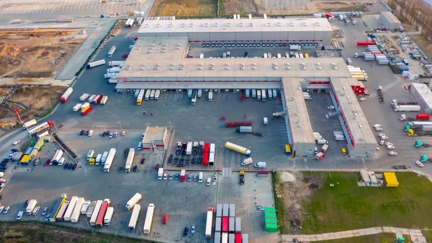 Aerial hyper lapse (hyperlapse - time lapse) of a large logistics park with a warehouse - loading hub. Semi-trucks with freight trailers standing at the ramps for loading/unloading goods  Royalty-Free Stock Footage #1052323507