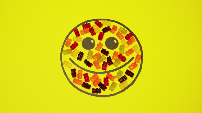 Smiley On Yellow Background Filled With Colored Candies. Candies In The Form Of Bears Move Inside The Smiley.
