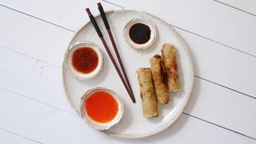 Fried Chinese Thai or Vietnamese traditional spring rolls or nems served on ceramic plate with sauces. Wooden background. Slow motion spin video