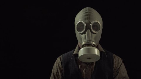 the man in the suit removes the gasmask. looking at the camera. 4K video. on a black background