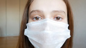 The girl in the medical mask is tired, looks forward, turns her head to the left. 4k video. Protecting against pandemics and epidemics.