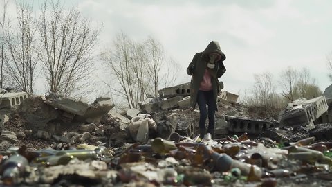 The girl in the gasmask stands in the middle of the landfill. overall plan. looks around, looking for food.