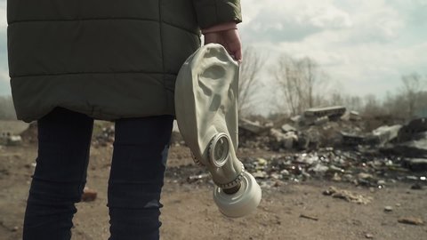 Girl holding a gasmask. rear view. goes in the direction of the landfill.