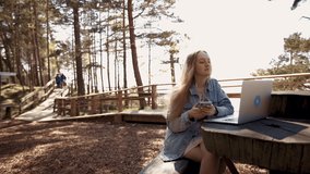 Young female blogger in earbuds records new video using laptop outdoors