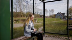 Young blonde female student attending online conference webinar and listens to lecture at bus stop during quarantine